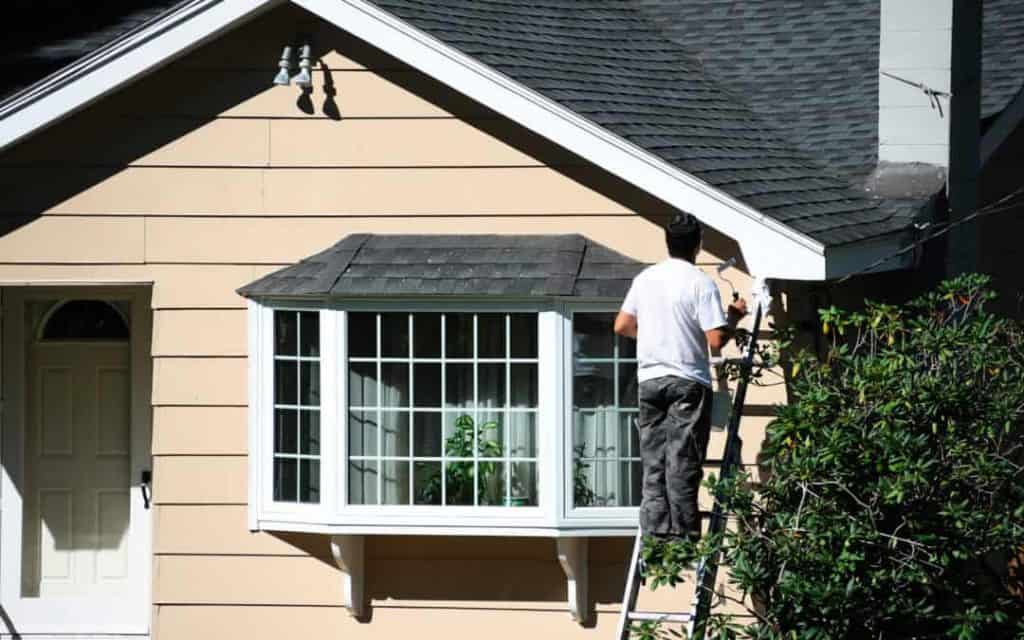 Man painting exterior wooden siding on a house
