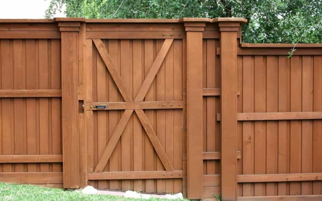 A Tall pressure treated pine privacy fence with a heavy gate stained a reddish shade of maple