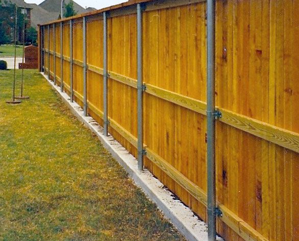 Steel supports in concrete support a wooden fence lining a playground
