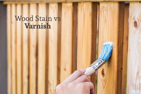 A person using a brush to add stain to a wood fence